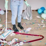 Woman with pushbroom cleaning mess of floor in room after party