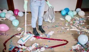 Woman with pushbroom cleaning mess of floor in room after party