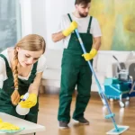 A couple cleaning a room with a mop and a painting on the wall