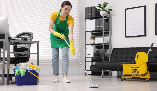 Cleaning service worker washing floor with mop bucket with supplies and wet floor sign in office