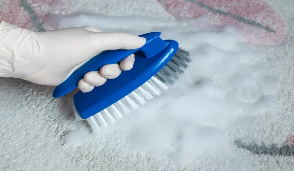 Blue brush on the carpet with hand in rubber glove cleaning