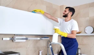 Man cleaning kitchen surface high up standing on a ladder. Cleaning service concept