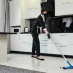 Professional cleaning service company employee in rubber gloves with a mop removes dirt from the floor and kitchen surfaces