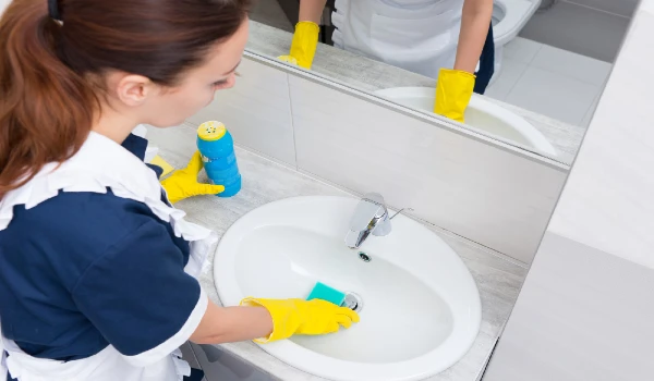 High angle view on housekeeper with yellow rubber gloves cleaning sink with blue sponge and scrubbing powder