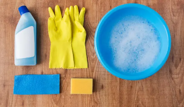 Housework, housekeeping and household concept - basin with cleaning stuff on wooden background