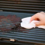 Dirty electric grill. Female hand wiping with cloth grill