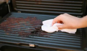Dirty electric grill. Female hand wiping with cloth grill