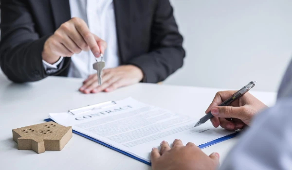Midsection of customer signing document while estate agent giving key over table